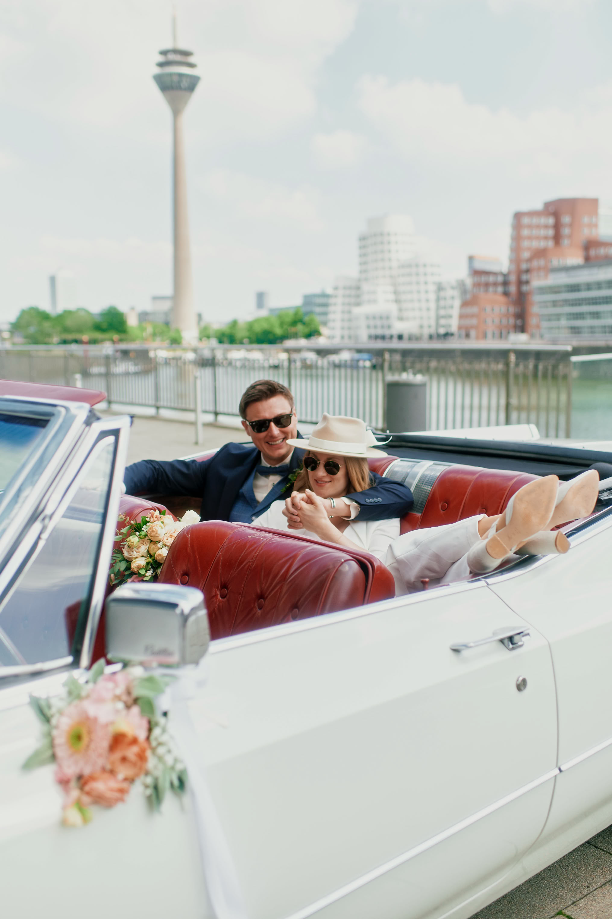 Cadillac DeVille Convertible Baujahr 1968 Hochzeitspaar genießt das wunderschöne rote Lieder Interieur. Hotel Hyatt im Medienhafen Düsseldorf mit Blick auf den Fernsehturm.