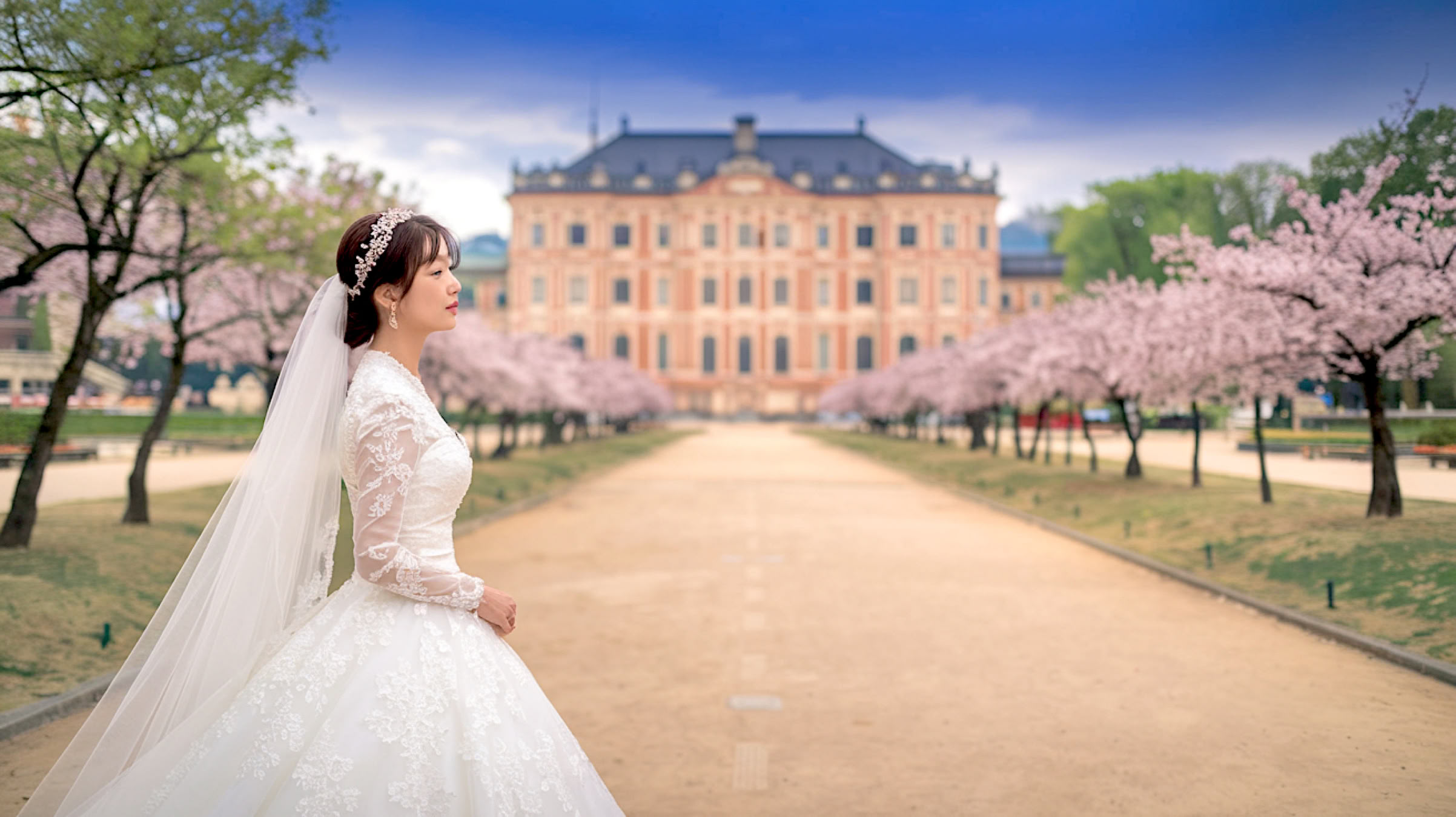 Hübsche Braut erwartet das Hochzeitsauto vor einem traumhaften Schloss